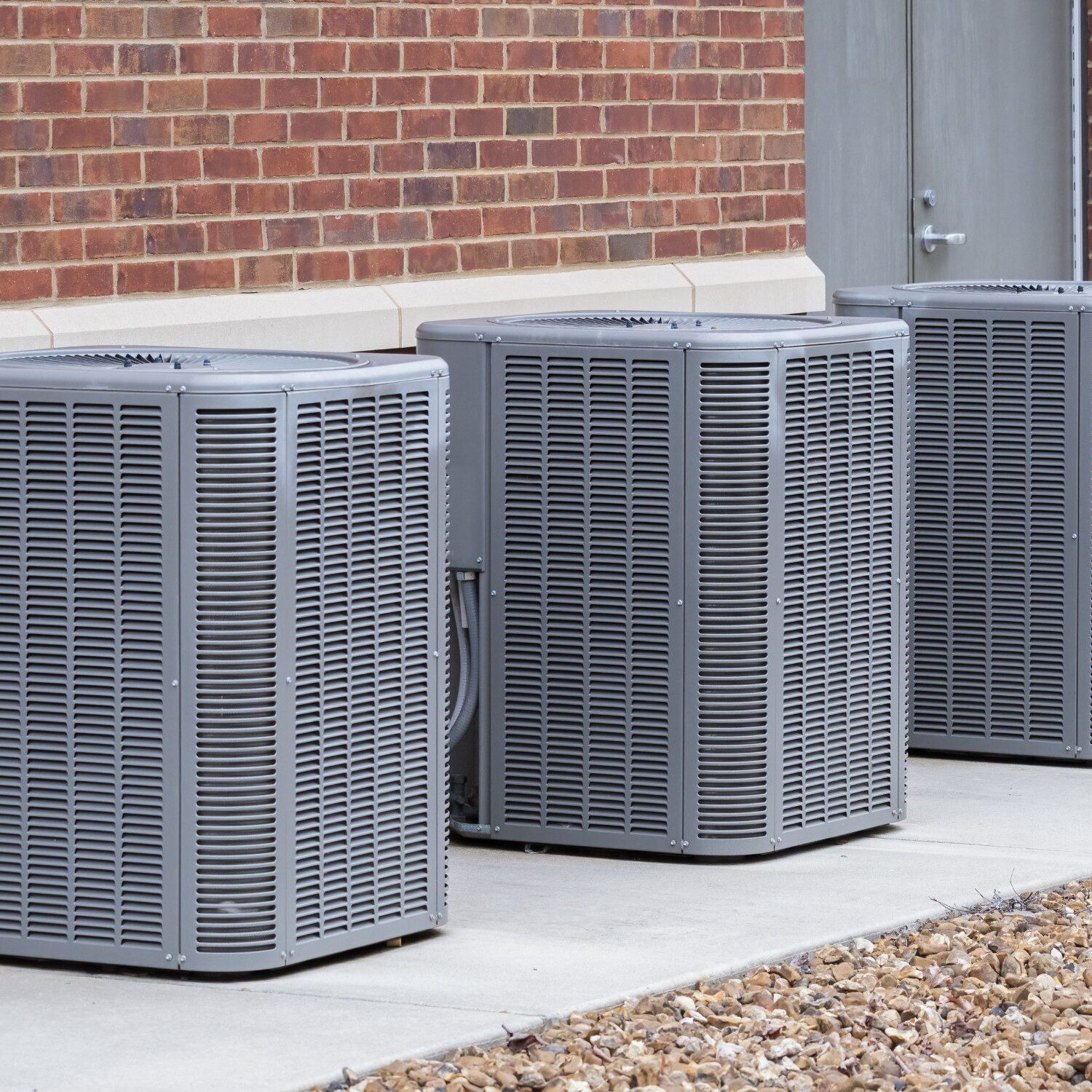 Three outdoor air conditioning units on ground.